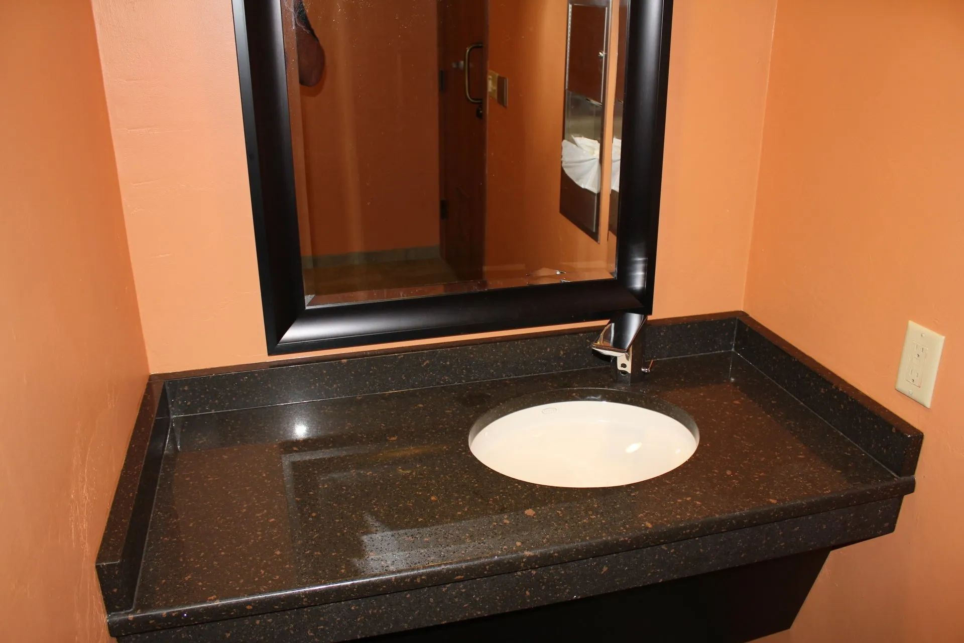 Bathroom vanity with black countertop, white sink, and mirror against orange walls.