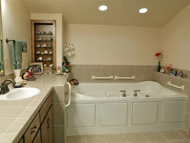 Bright bathroom with a white bathtub, beige walls, vanity sink, and recessed ceiling lights.