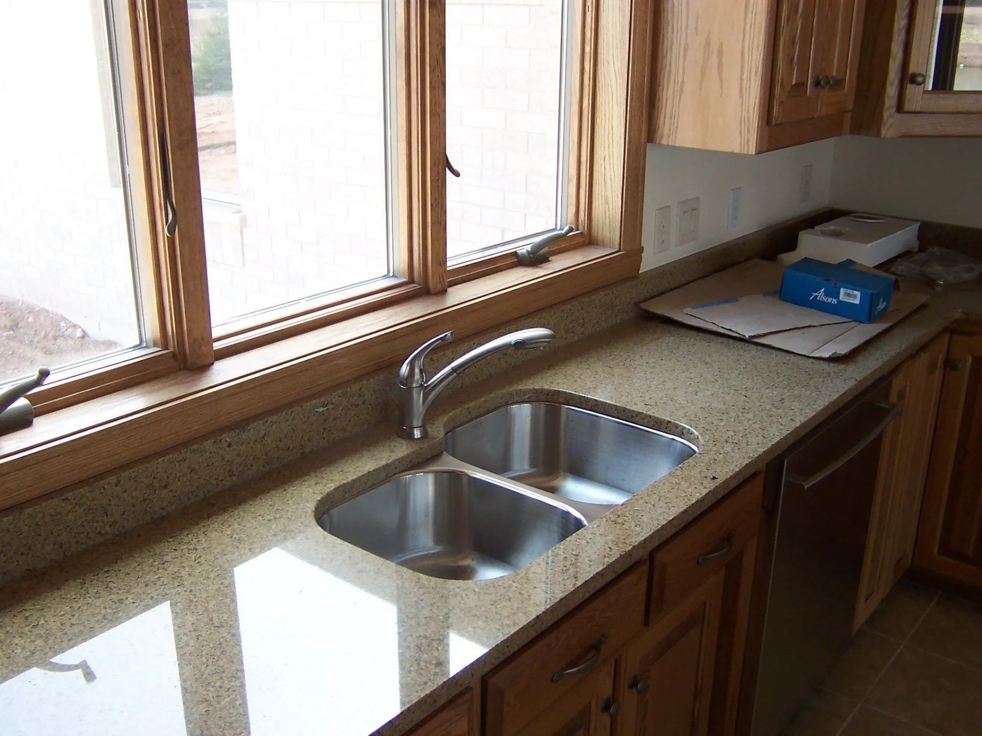 Kitchen countertop with double sink, faucet, and wooden cabinets beside a window.
