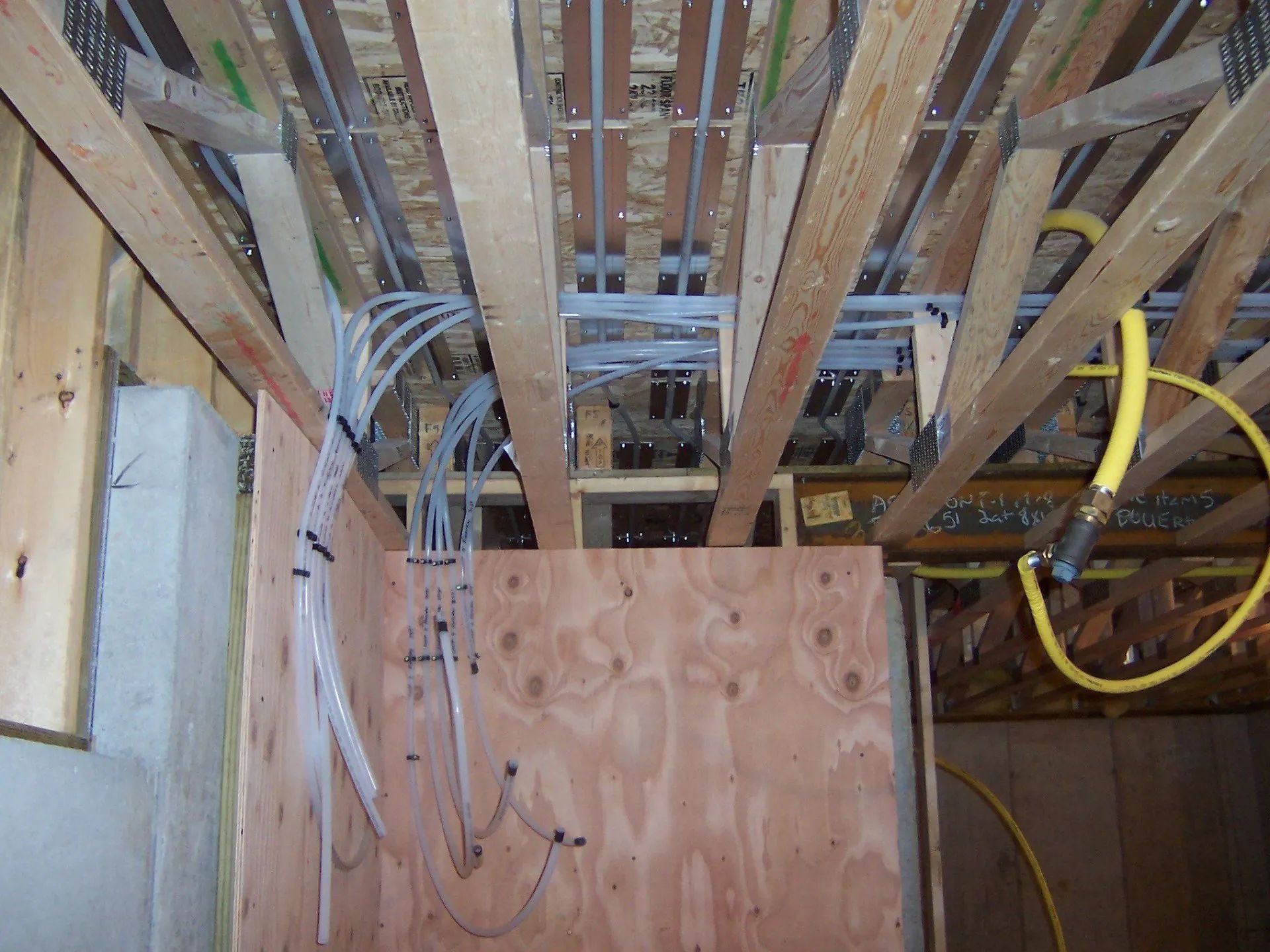 Exposed ceiling joists and wiring in unfinished room with plywood panel and yellow conduit hose