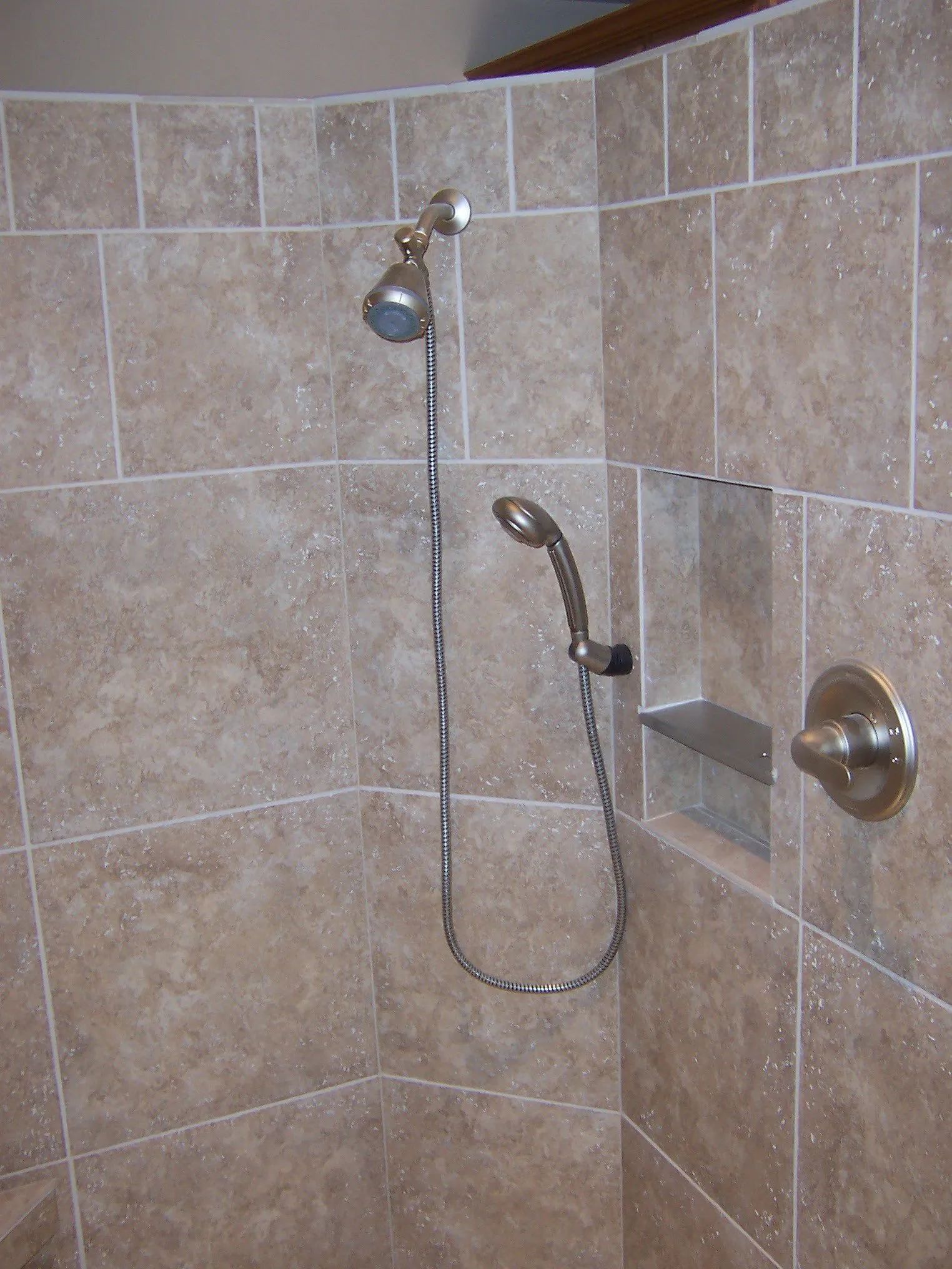 Tiled shower stall with wall-mounted showerhead and handheld shower wand attached to a grab bar.