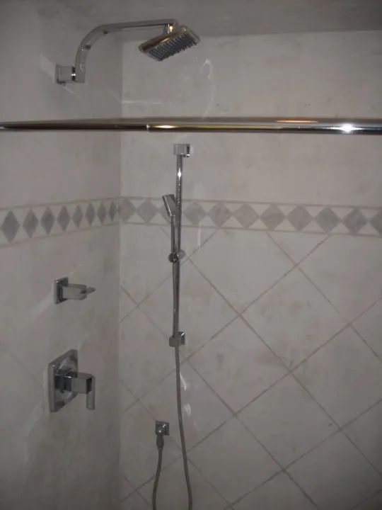 Tiled bathroom shower with chrome faucet, handheld showerhead, and wall-mounted grab bar
