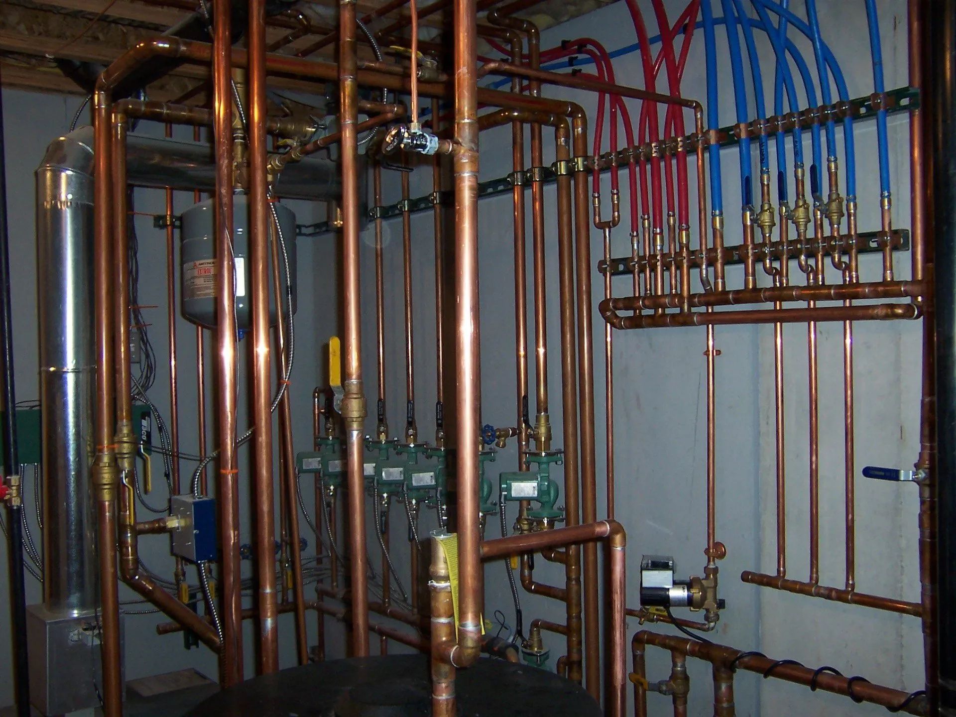 Basement utility room with copper pipes, valves, and blue and red tubing on the walls