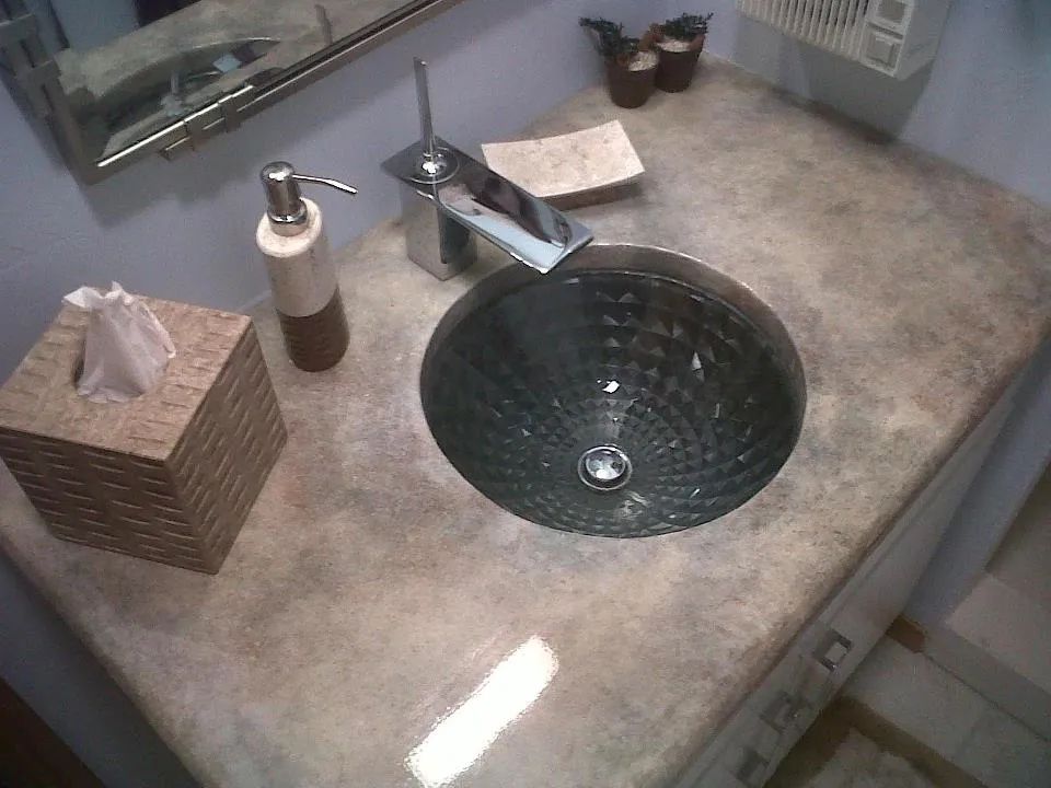 Bathroom countertop with a glass vessel sink, faucet, soap dispenser, and tissue box on a stone vanity.