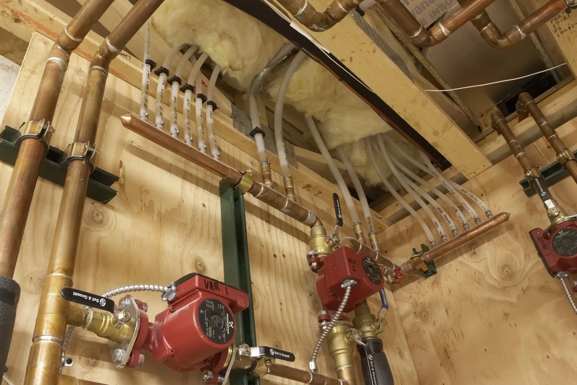 Red fire sprinkler pipes and valves mounted on a wooden ceiling in a utility room