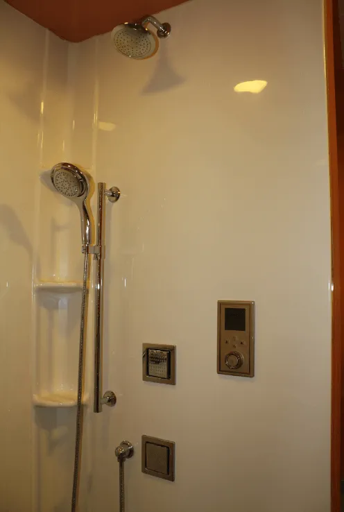 Bathroom shower with glass door, handheld showerhead, and wall-mounted controls.