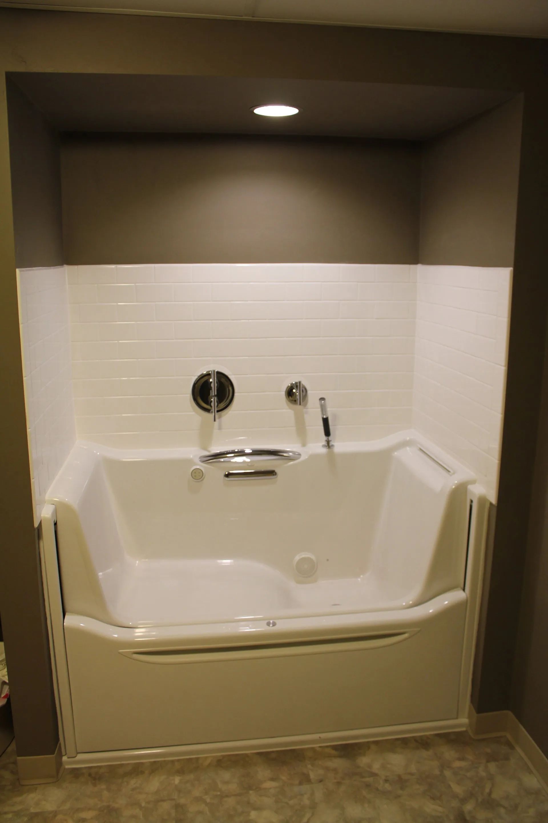 Built-in white walk-in bathtub with grab bar and recessed light in a tiled alcove