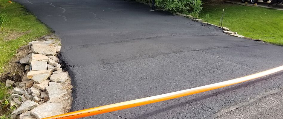 A black asphalt driveway with a yellow pole in the middle of it.