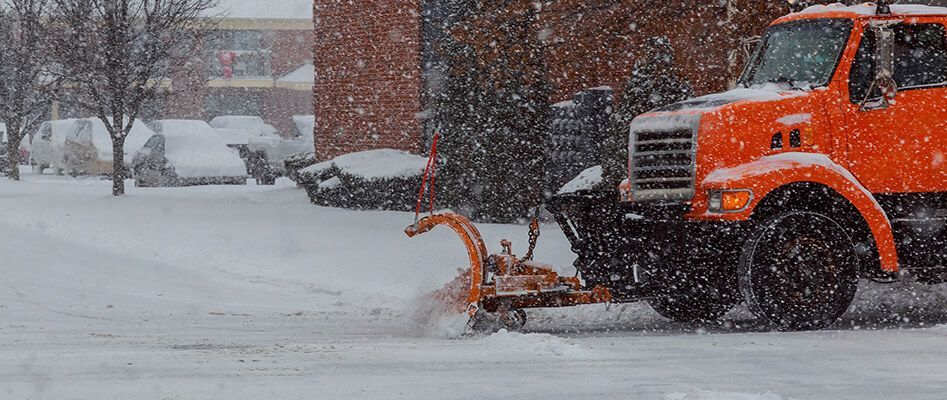 An orange snow plow is clearing snow from a parking lot.