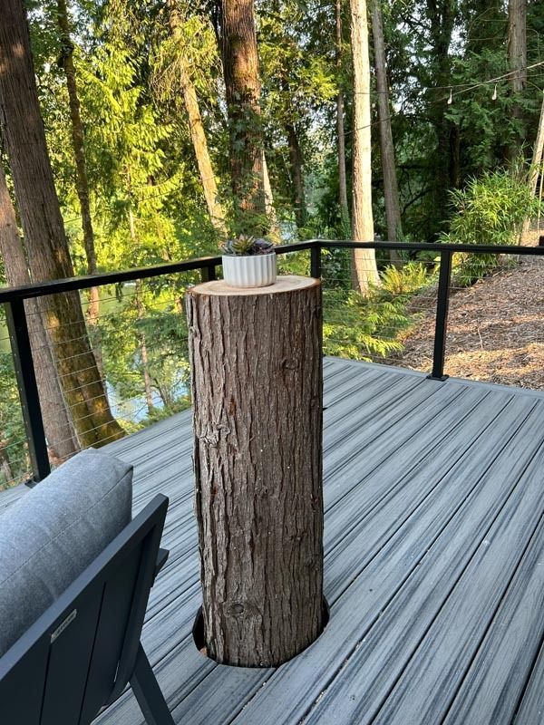 Wooden stump table with a white dish, on a deck overlooking trees and water.