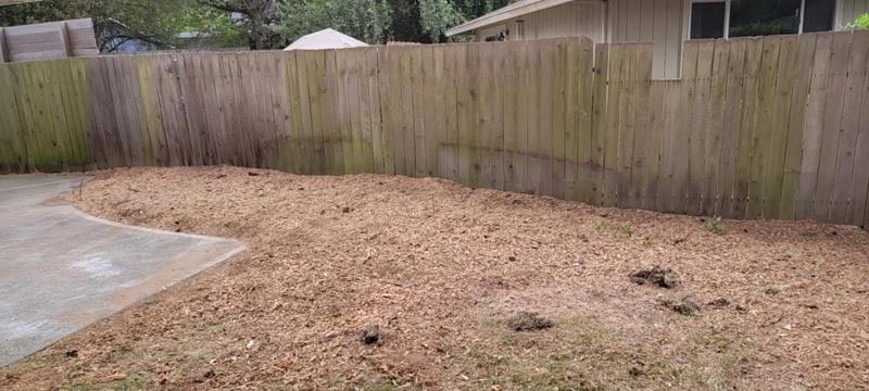 A backyard with wood chip ground cover, wooden fence, and concrete patio.