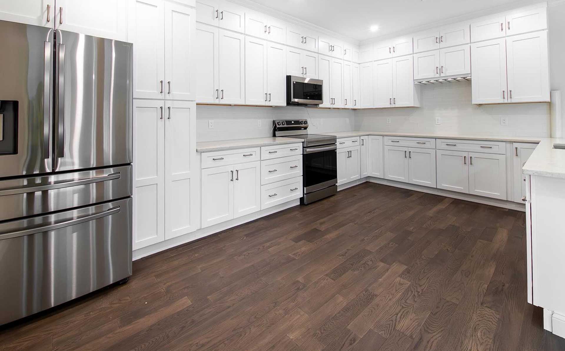 White kitchen with stainless steel appliances and dark wood flooring.