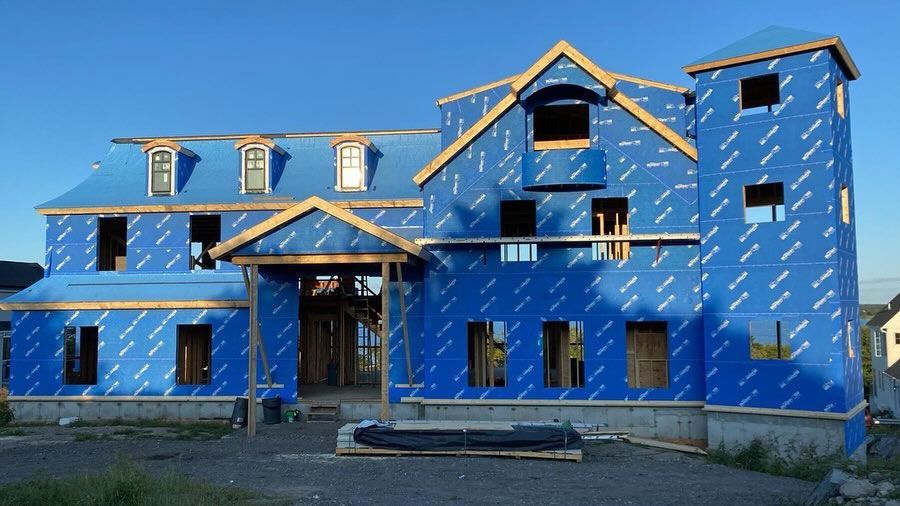 A house under construction, framed with wood and covered in blue weather-resistant barrier.