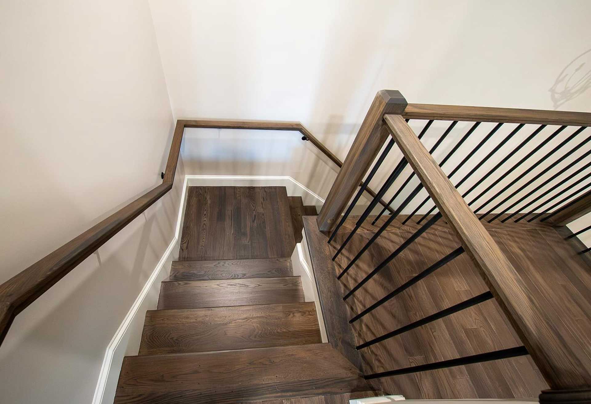 Wooden staircase with dark brown treads and handrails; white walls, metal railing.