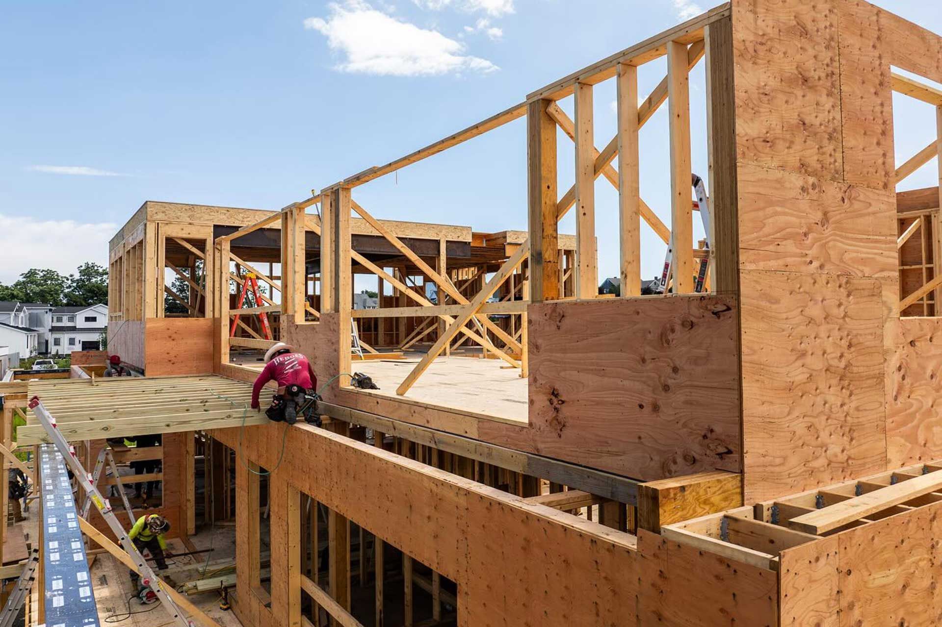 Construction workers framing a building with wooden structures, viewed from above on a sunny day.