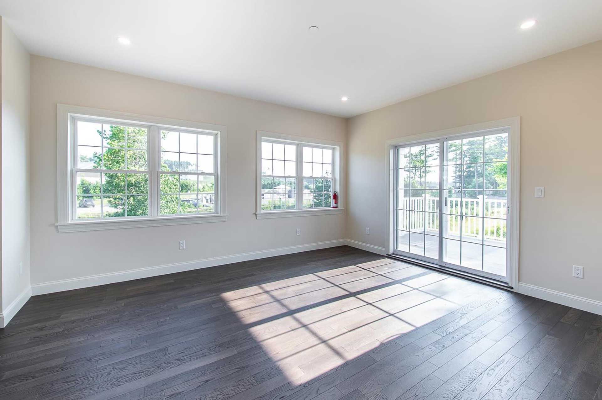 Empty room with dark wood floor, white walls and trim, large windows, and sliding glass door.