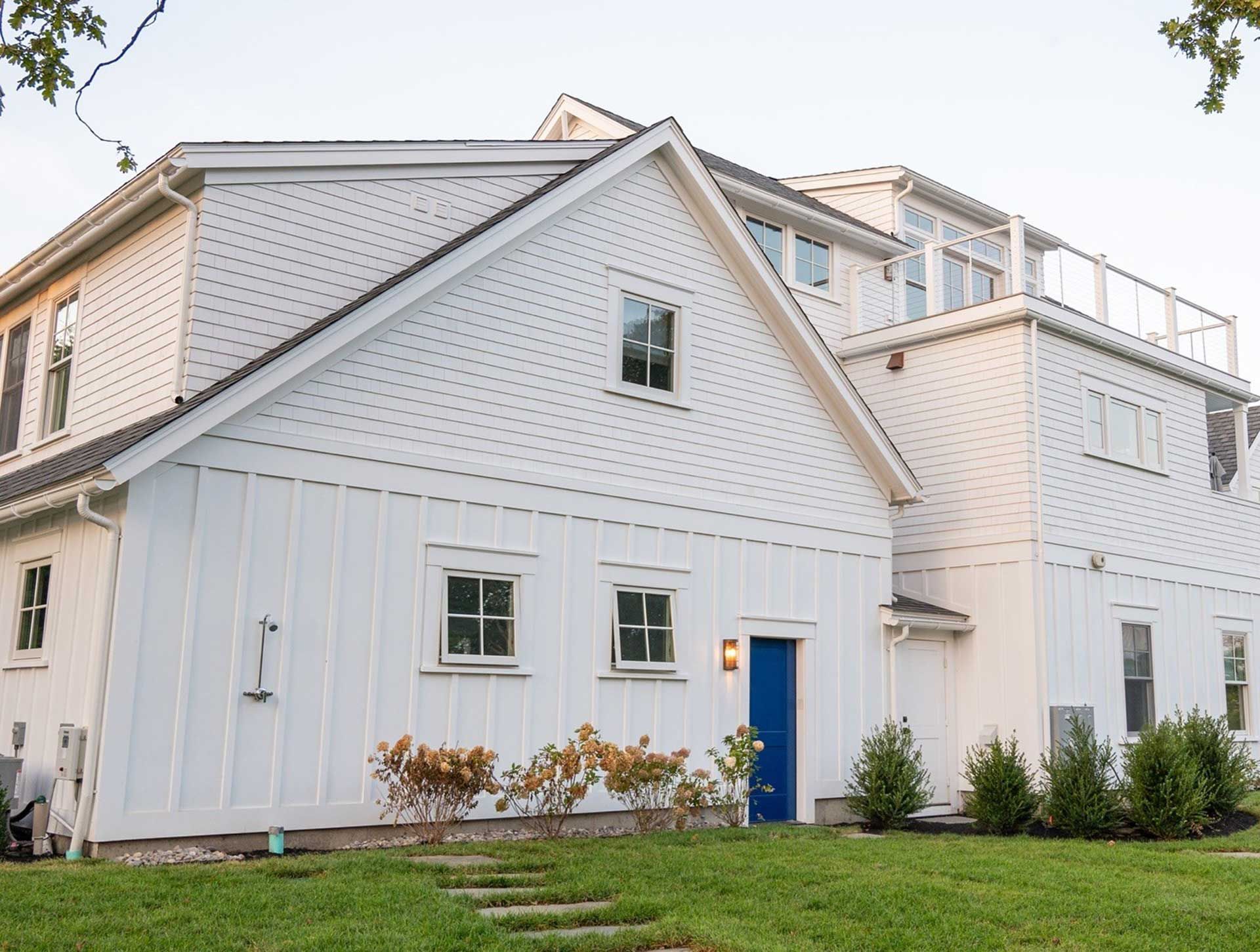 White multi-story house with blue door, grass lawn, and small bushes.