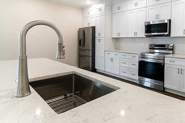 Modern white kitchen with stainless steel appliances, sink, and faucet.