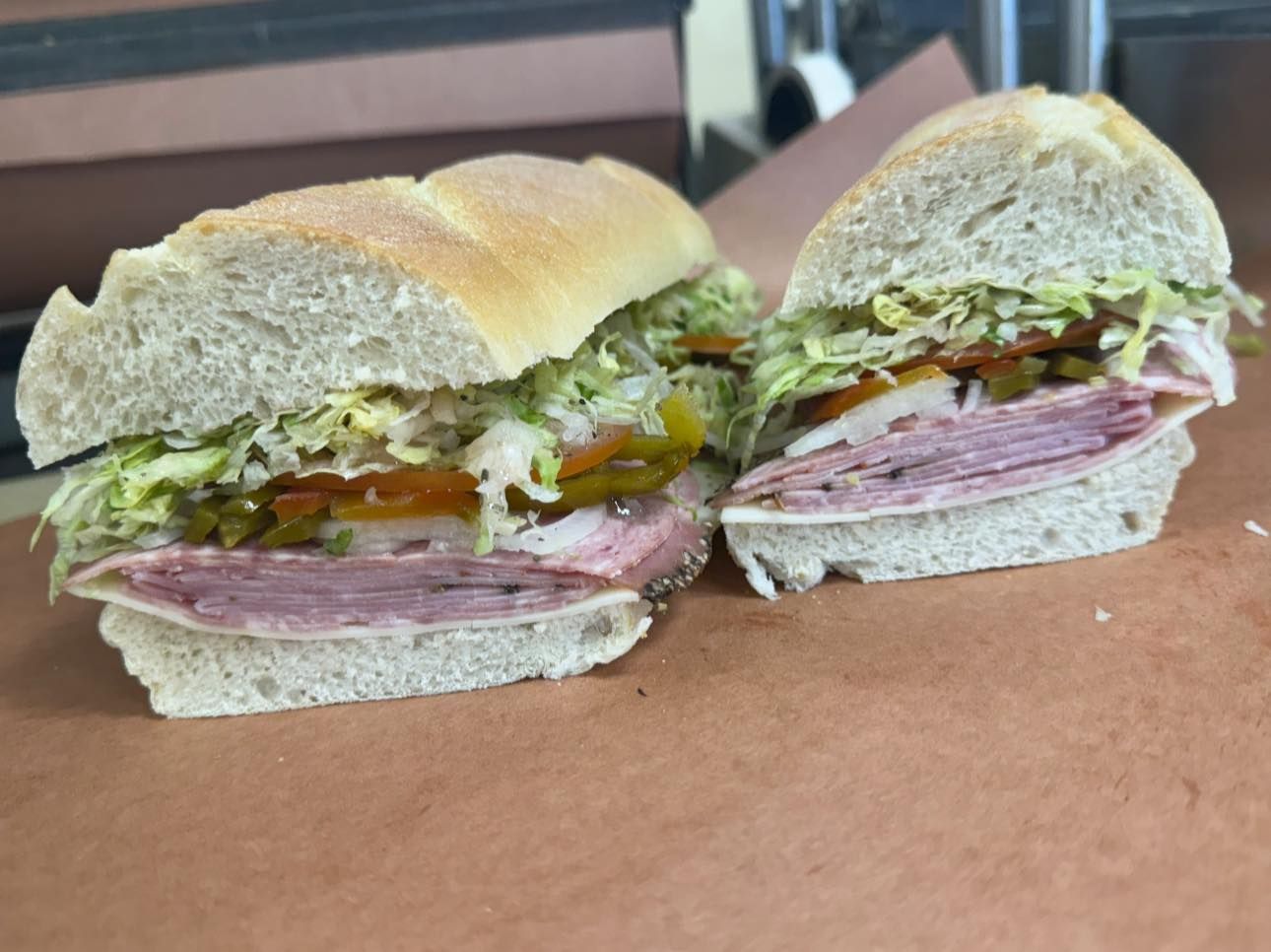 Two subs cut in half, stacked with lettuce, tomato, ham, and cheese on paper.