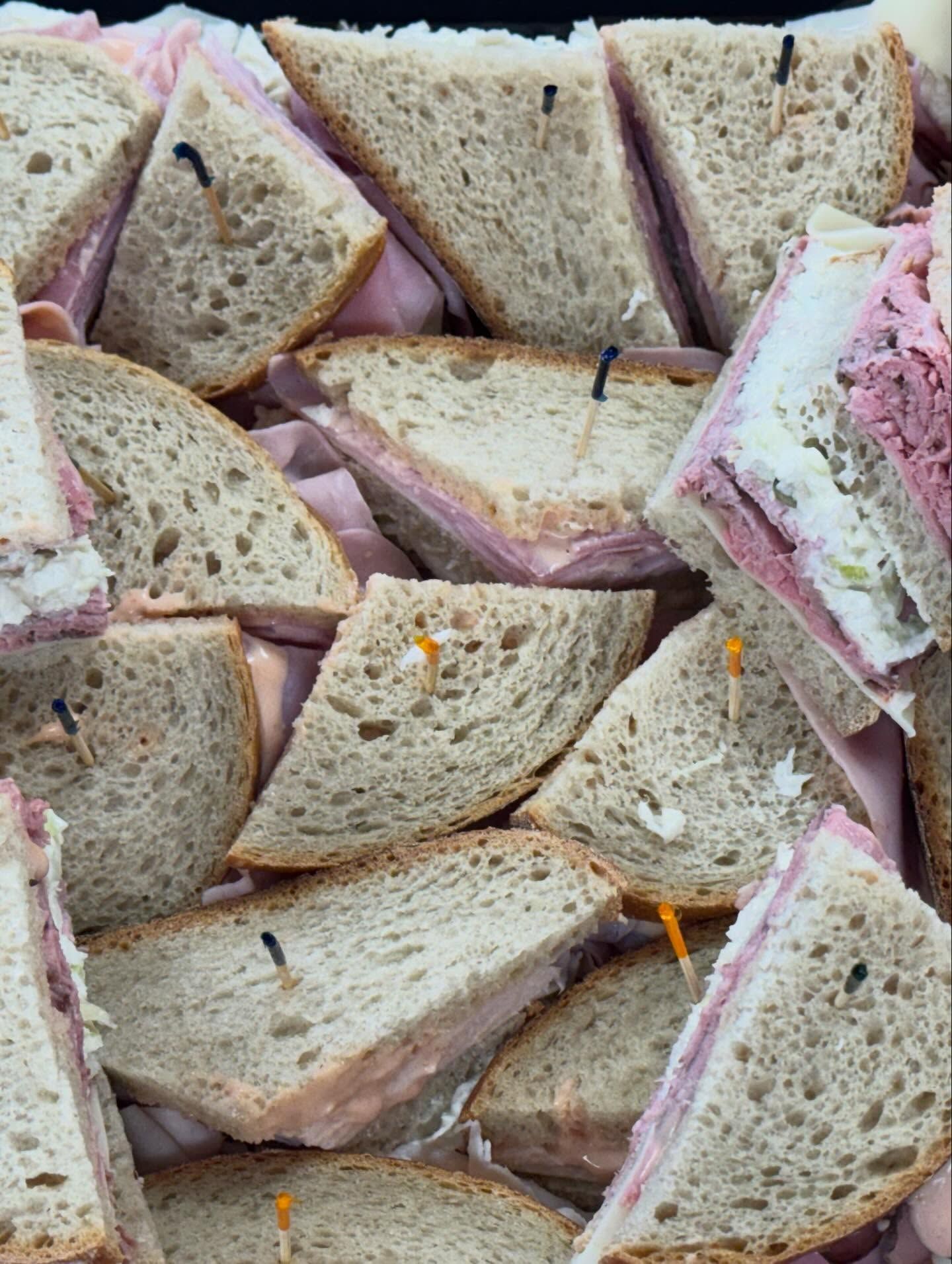 Assorted triangular tea sandwiches with pink filling, stacked closely together on a tray.