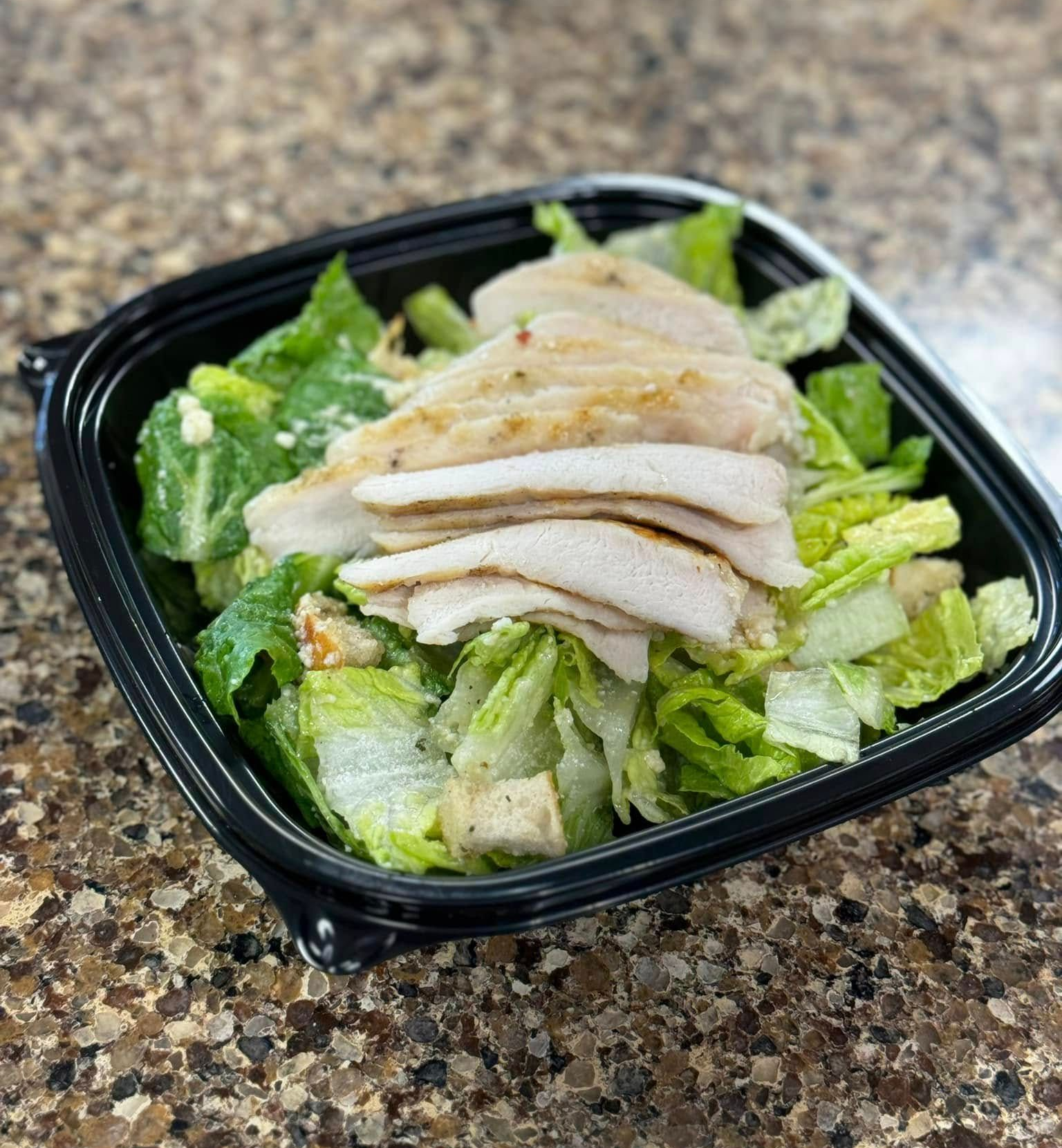 Chicken salad in a black takeout container with lettuce on a speckled countertop