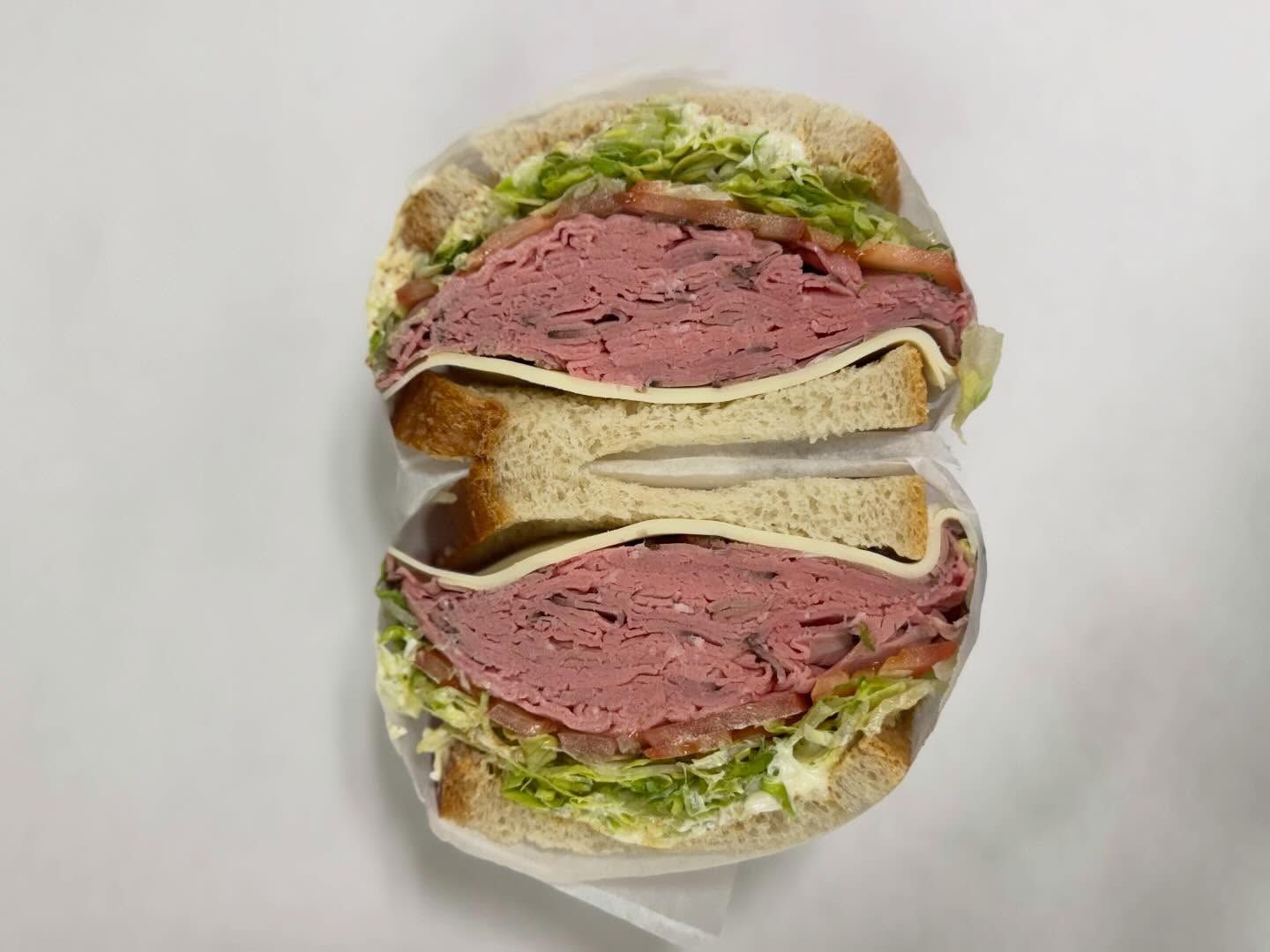 Cross-section of a sandwich with pink meat, lettuce, and white bread against a white background.