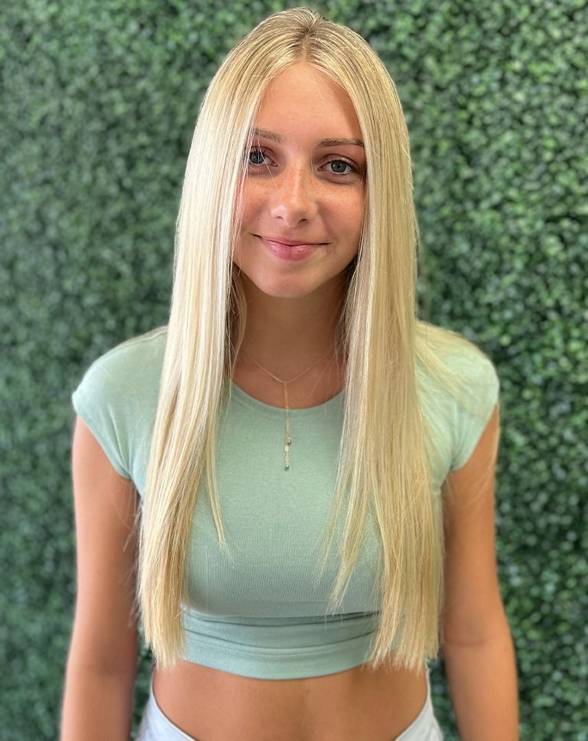 Blonde girl with long, straight hair, wearing a light green crop top, smiling, in front of a green background.