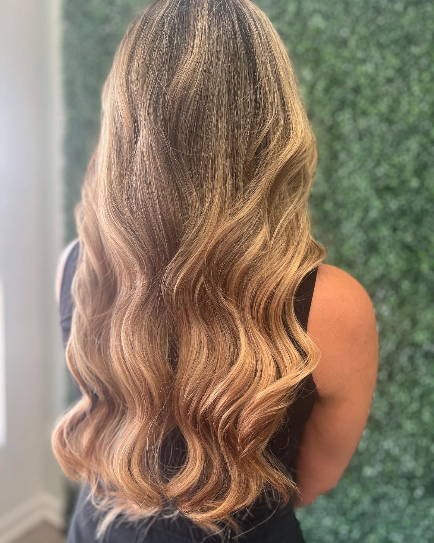 Woman with long, wavy, ombre hair; blonde to brown. Green background.