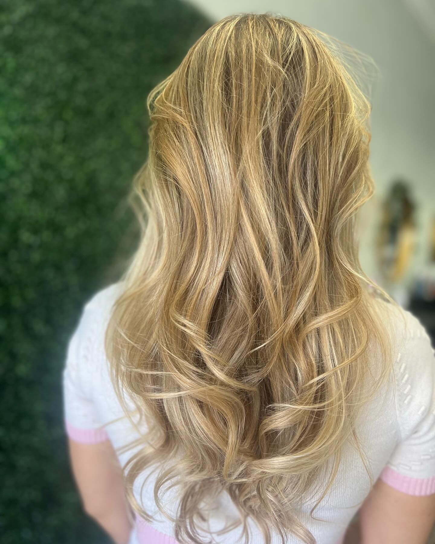 Woman with long blonde and crimped hair, wearing a white shirt with pink trim.