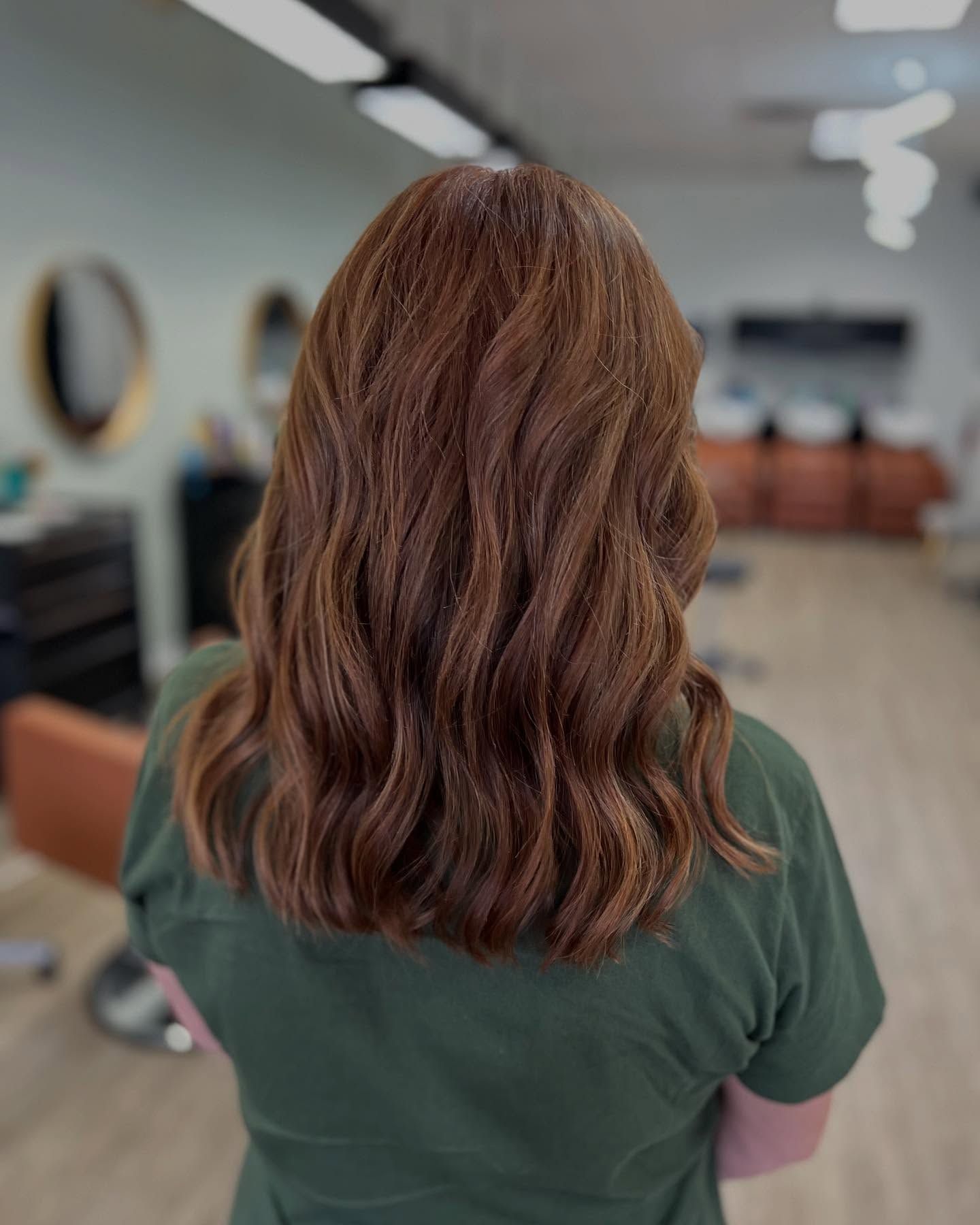 Woman with wavy, reddish-brown hair; in a hair salon, wearing a green shirt.