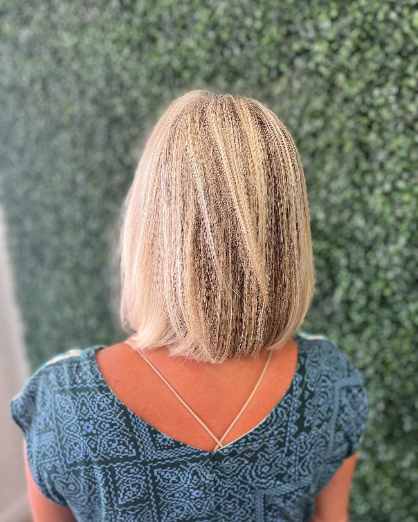 Blonde bob haircut from the back; woman in teal top against a green backdrop.