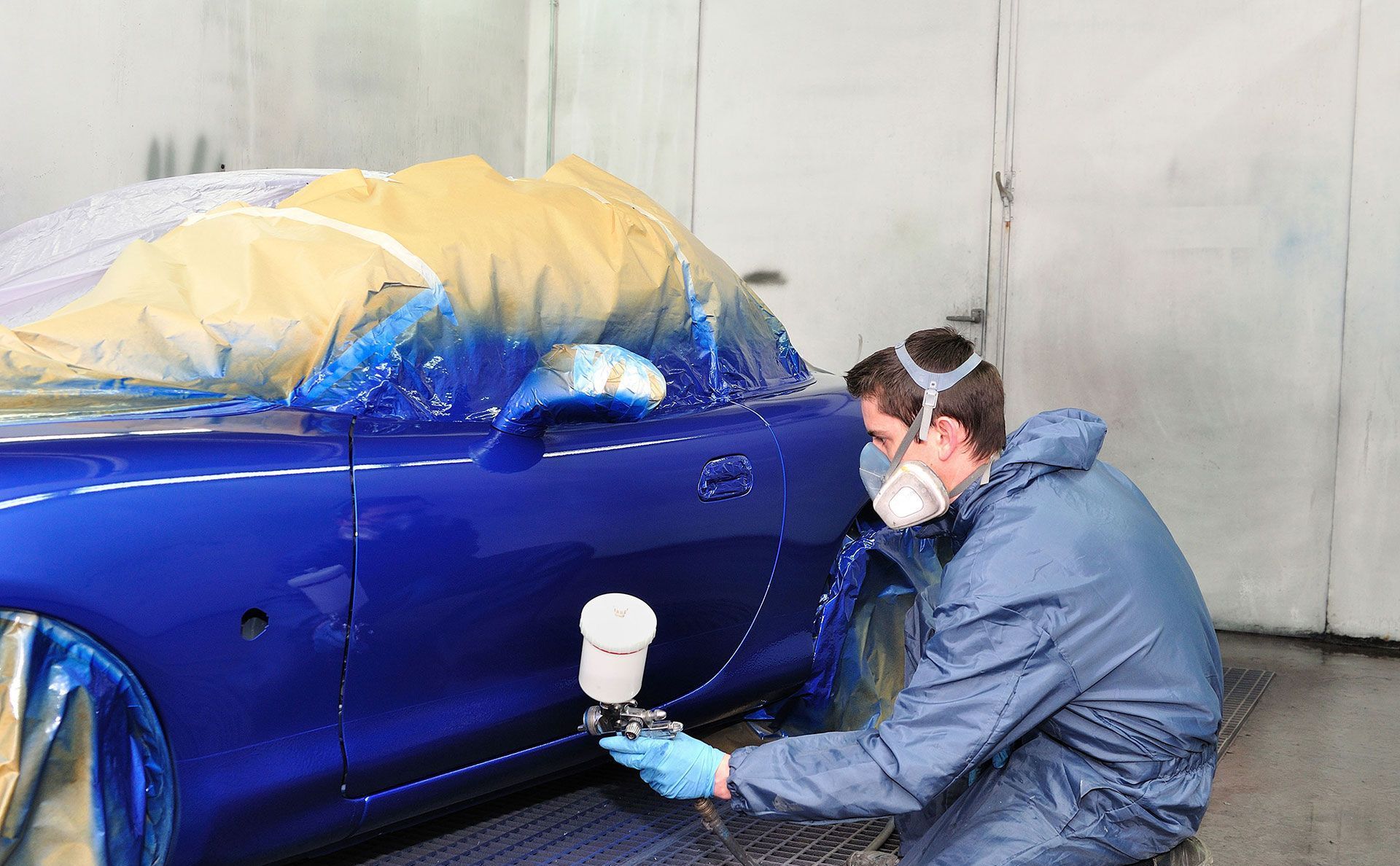 A man wearing a mask and gloves is spray painting a car.
