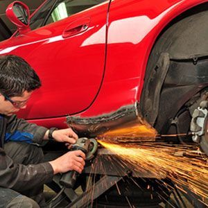 A man is grinding the side of a red car.