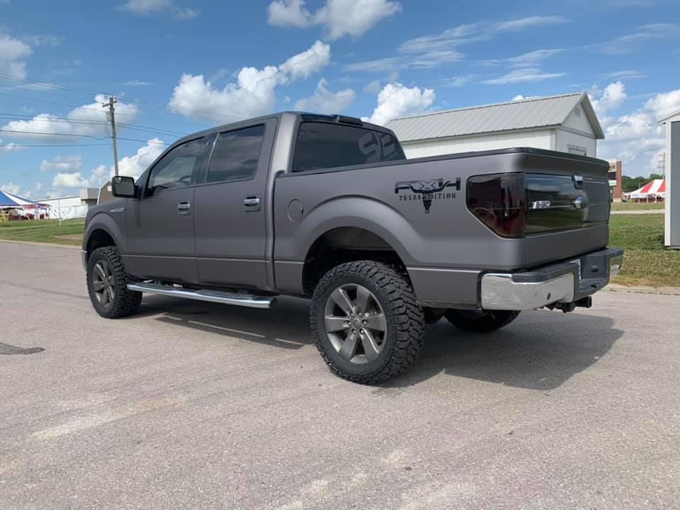 Gray lifted pickup truck parked on pavement under a partly cloudy sky