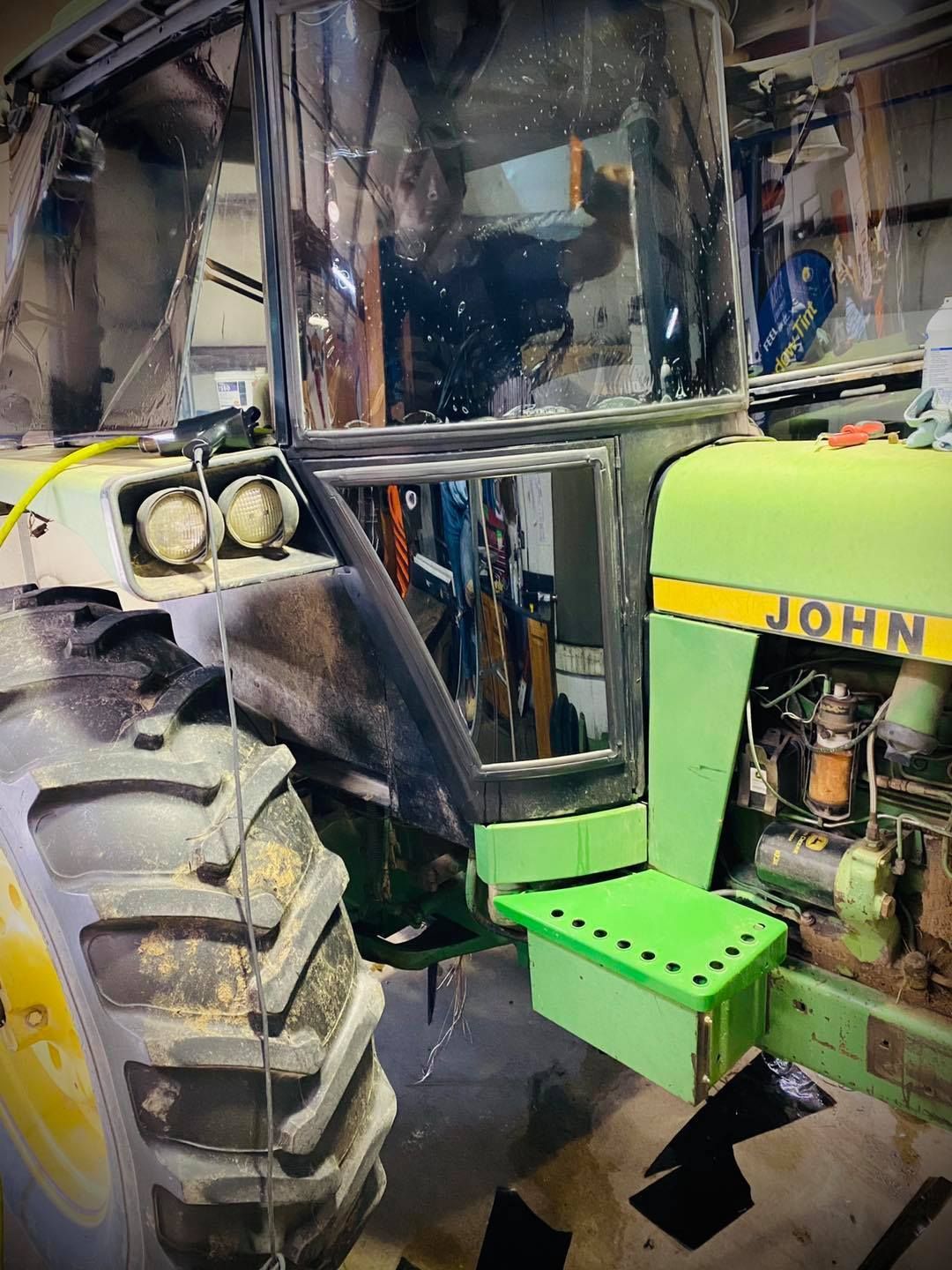 Green John Deere tractor cab with large front tire in a workshop garage
