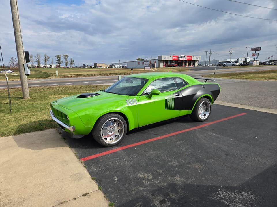 Bright green classic muscle car parked in a lot near a road and grassy field