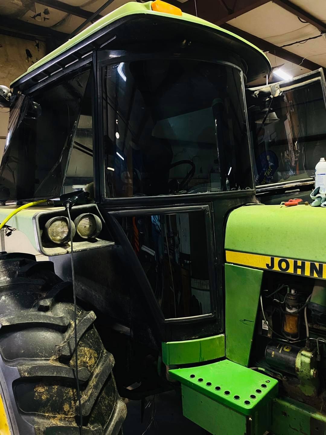 Yellow-and-green tractor cab with large tire in a dim garage or workshop