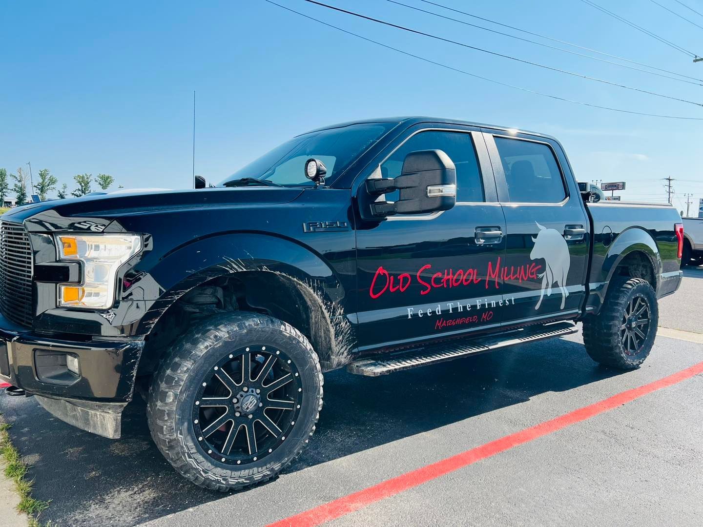 Black lifted pickup truck with red logo parked on a roadside under a clear blue sky