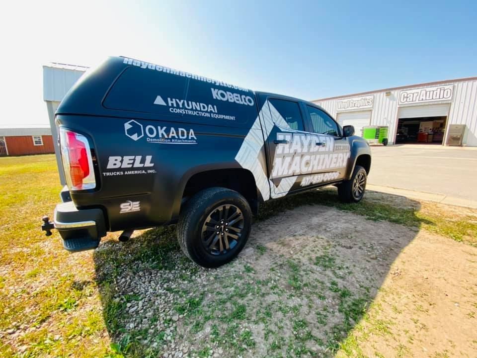 Black off-road SUV with racing decals parked on a dirt lot near industrial buildings