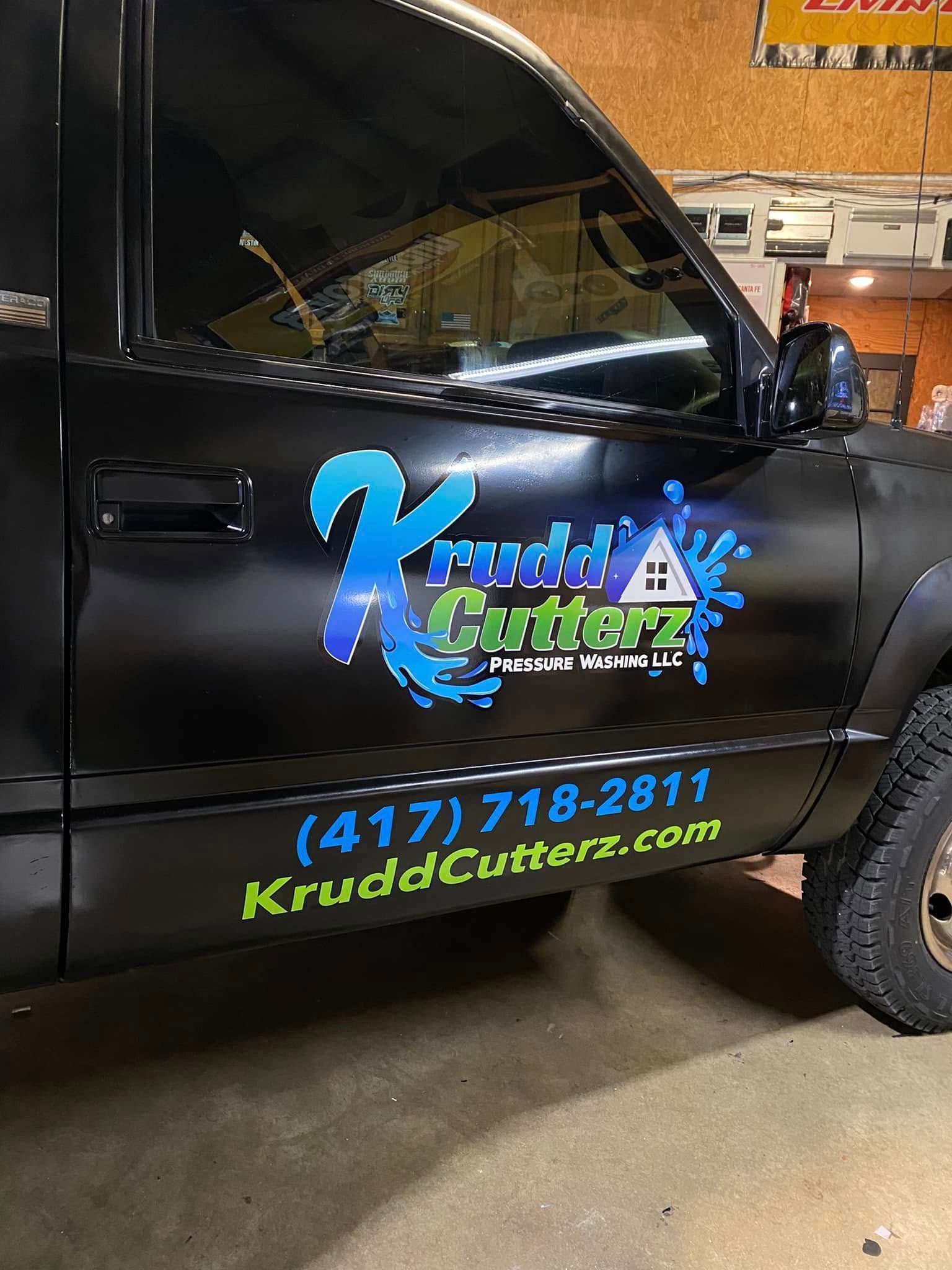 Black business van door with bright blue and green Kudd Cuts logo, phone number, and website on the side