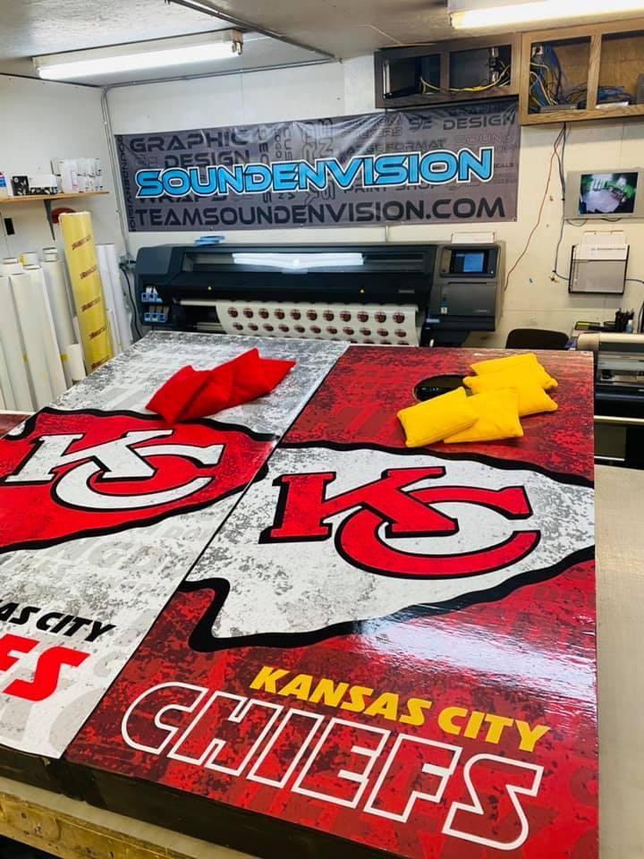 Kansas City Chiefs-themed floor mats in a shop, with red, white, and gold logo designs on display.
