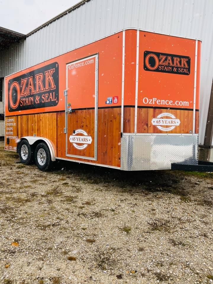 Orange Ozark Fence & Seal trailer with black-and-white branding, parked on gravel beside a building.