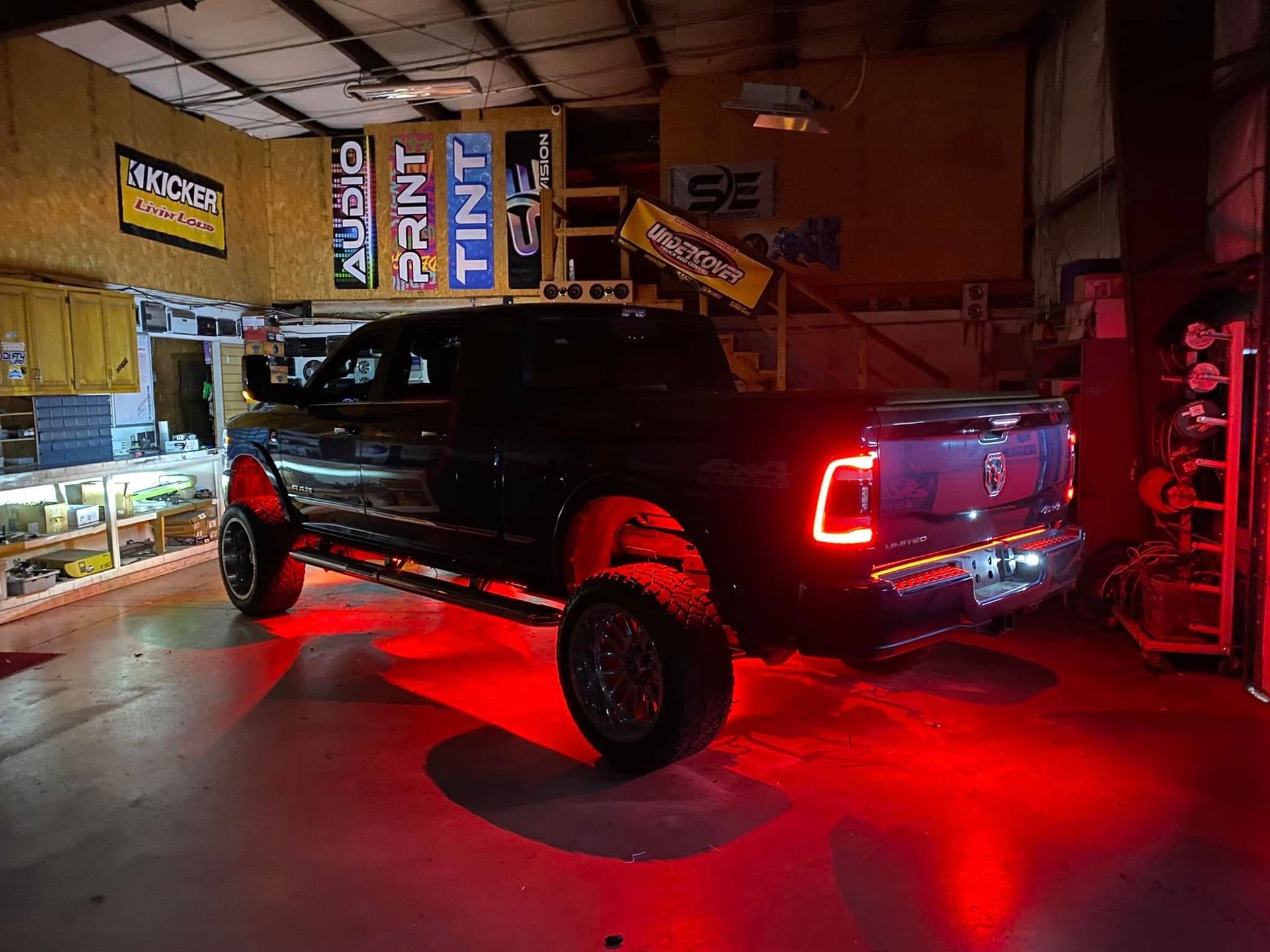 Black pickup truck with red underglow lights parked inside a garage or workshop.