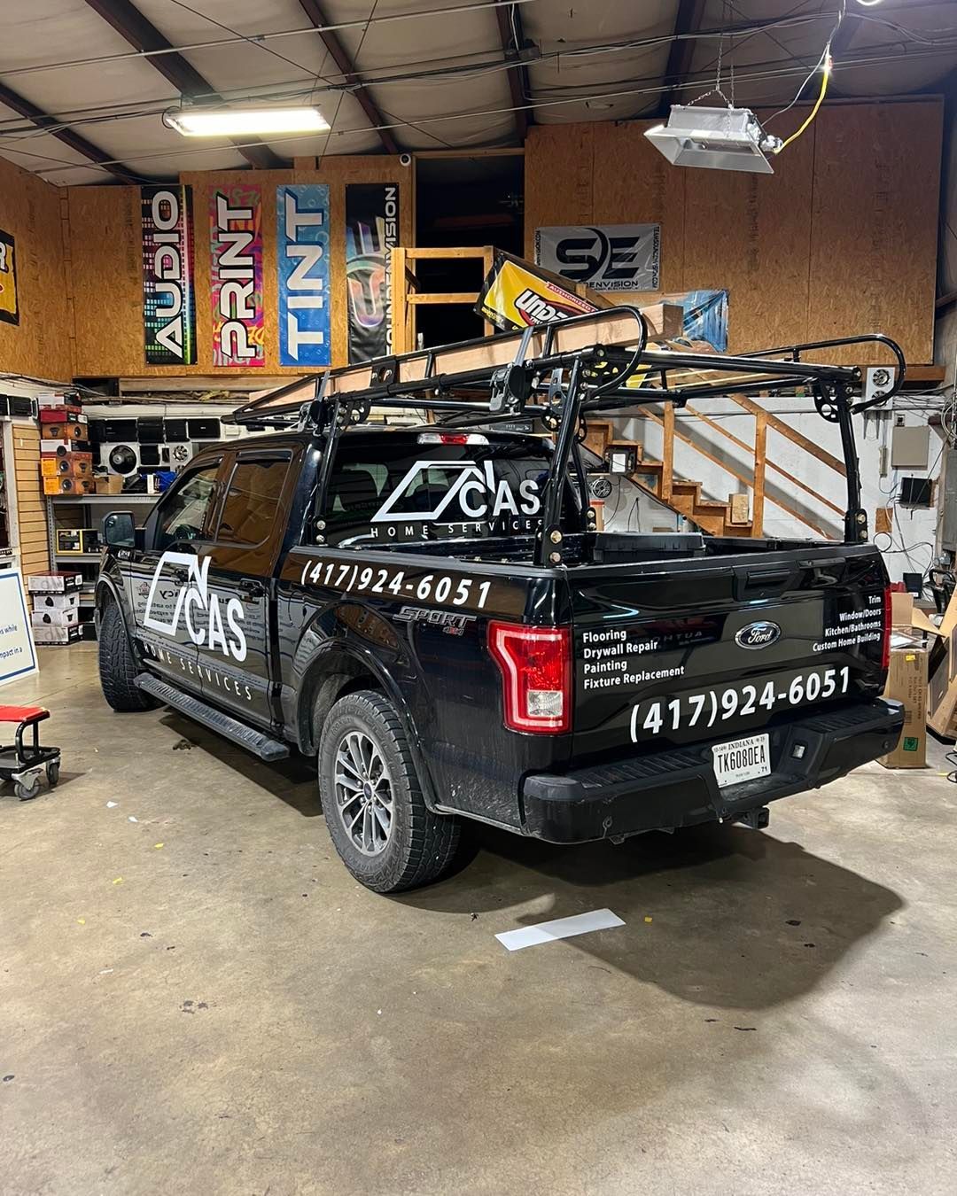 Black CAS service pickup truck in a garage, loaded with metal frames and tools, rear view