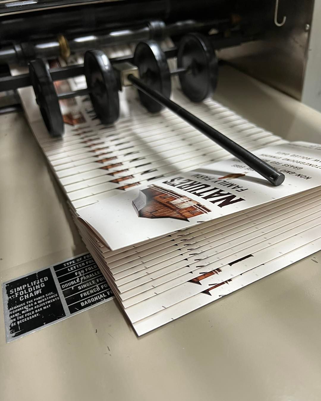 Printing press feeding white brochures with brown-and-black design through rollers