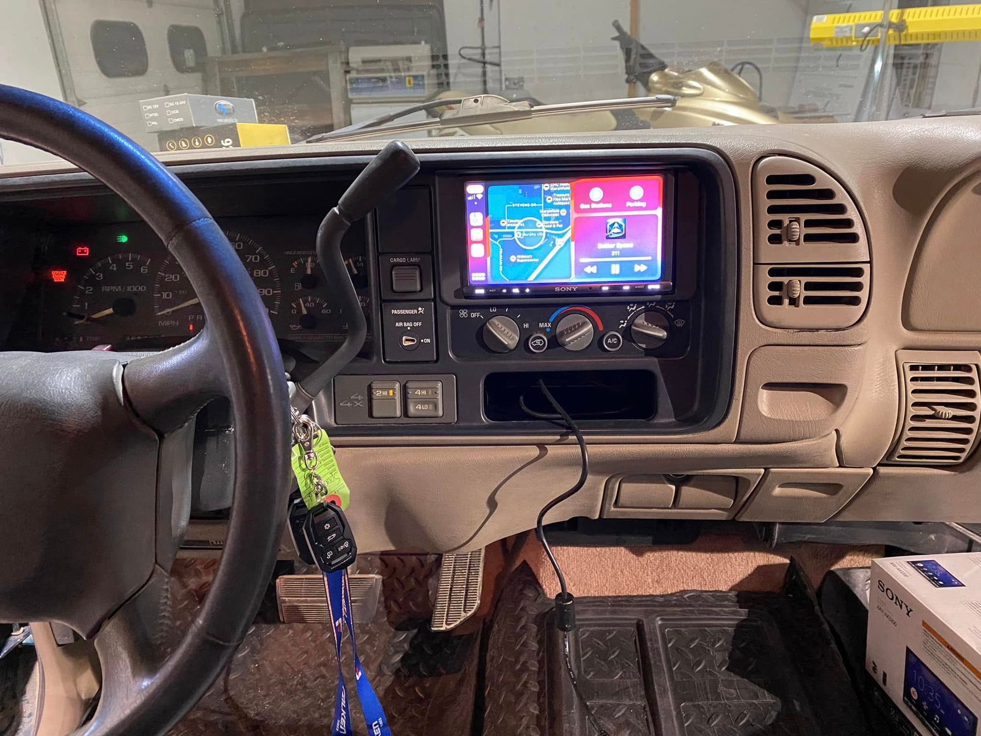 Car dashboard with steering wheel, center touchscreen, and climate controls; workshop garage setting.
