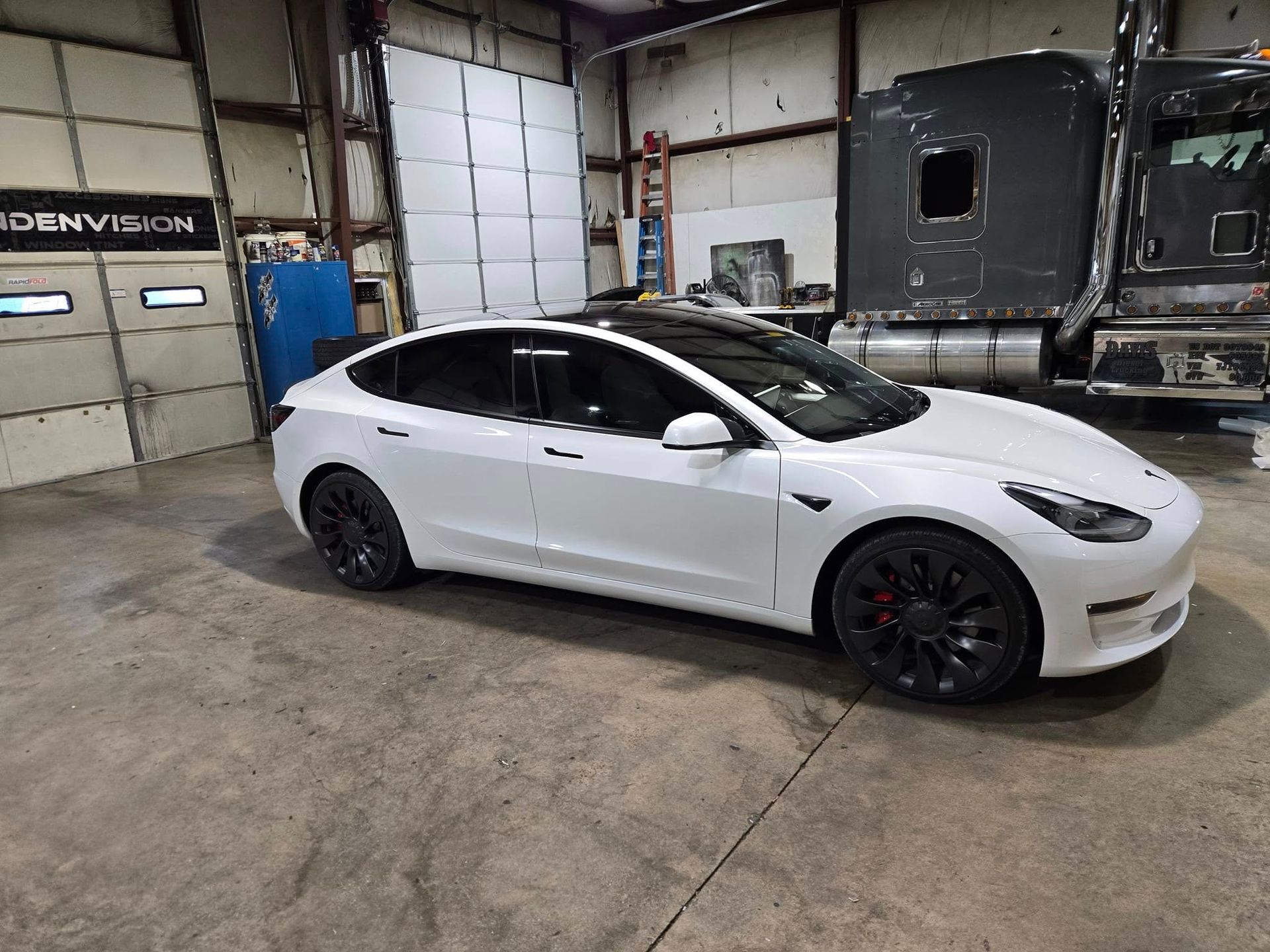 White Tesla sedan parked inside a garage with concrete floor and large doors