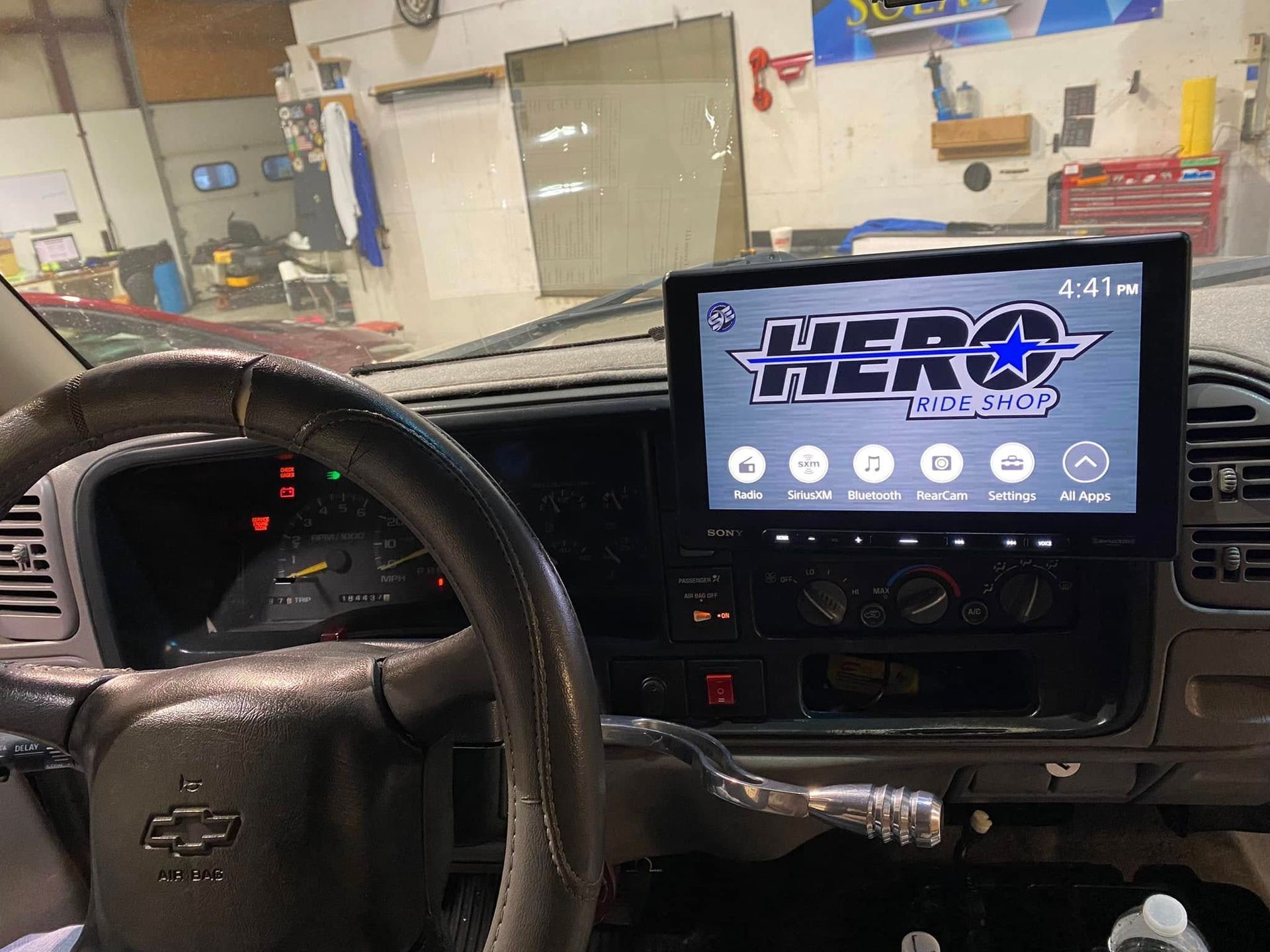 Car interior with steering wheel and a dash-mounted screen showing a logo in a garage.