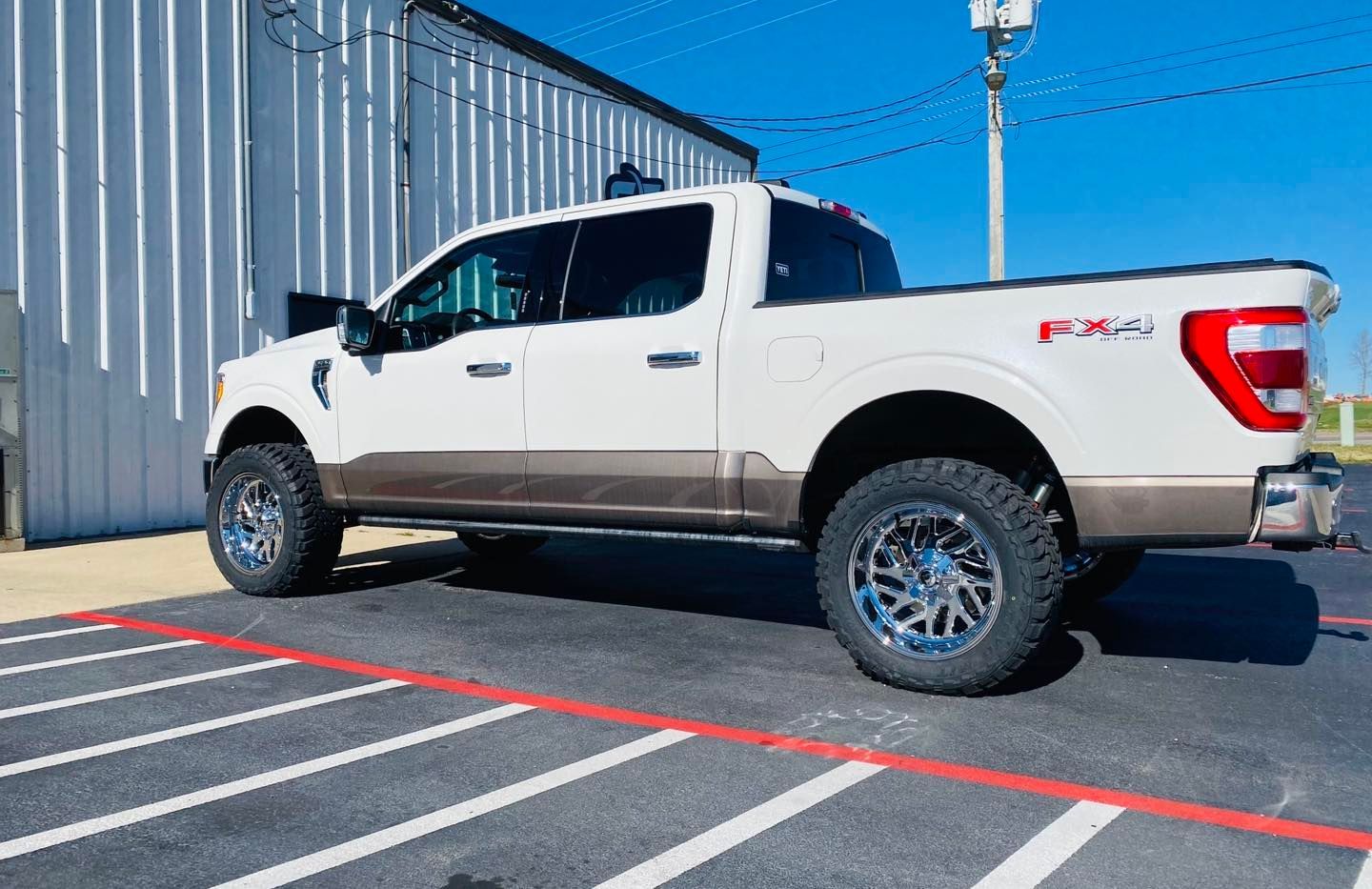 White Ford F-150 pickup parked beside a metal building in a striped parking lot, shown in side view.