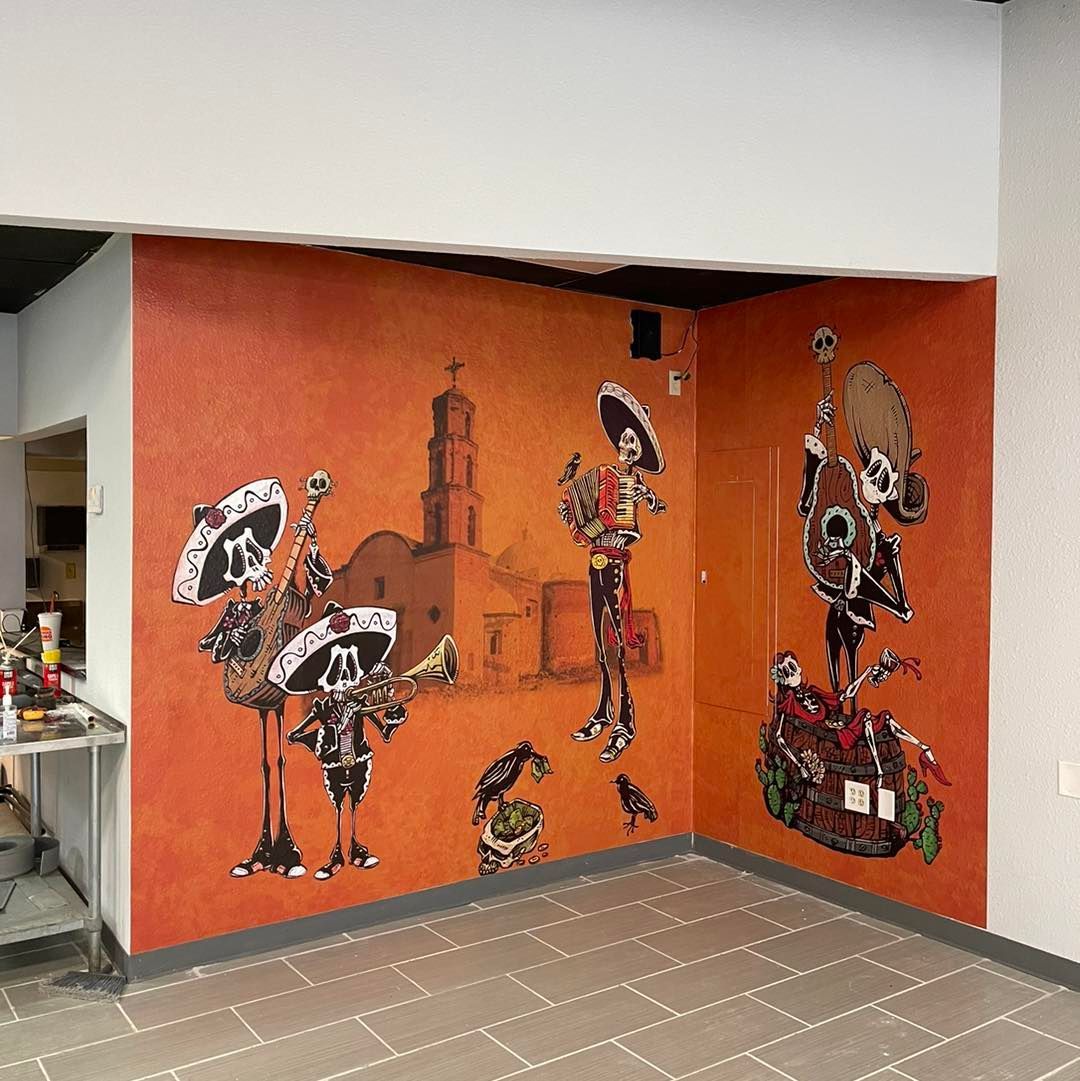 Orange mural with Día de los Muertos skeleton figures on a wall in a hallway